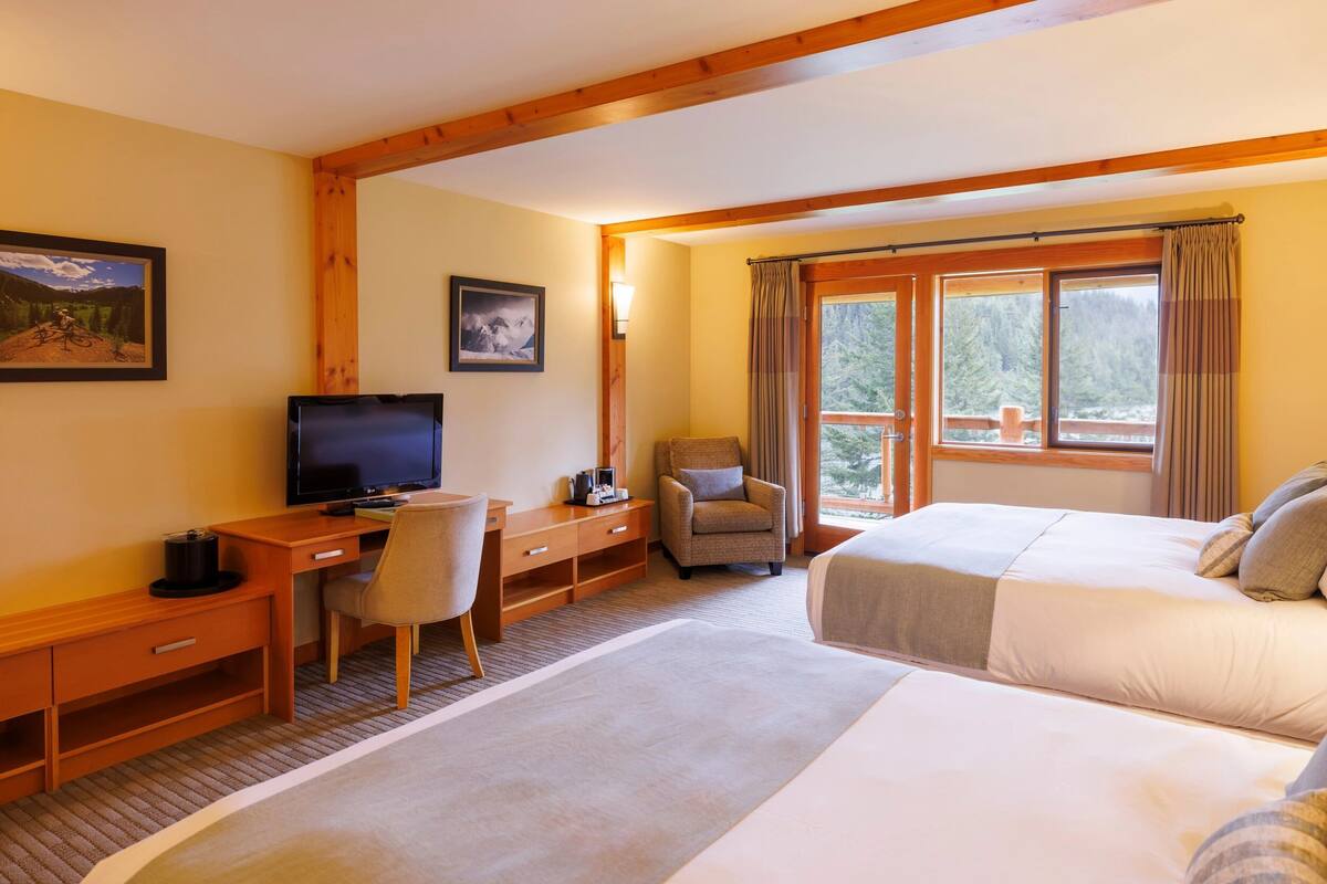 A hotel room with a bed, a desk with a chair, a television, and a window with curtains.