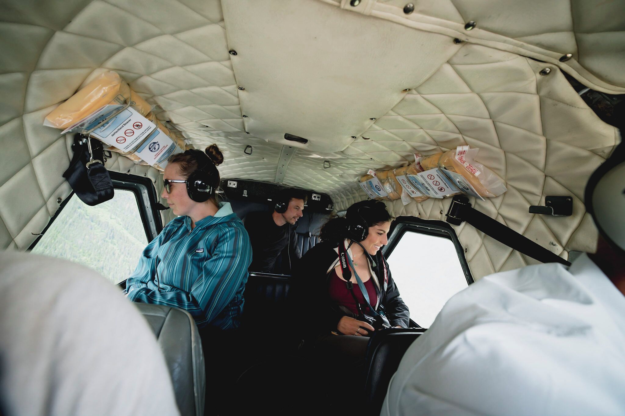 A vehicle interior with passengers wearing headsets, a quilted ceiling, and various items on the seats.