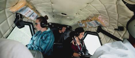 A vehicle interior with passengers wearing headsets, a quilted ceiling, and various items on the seats.