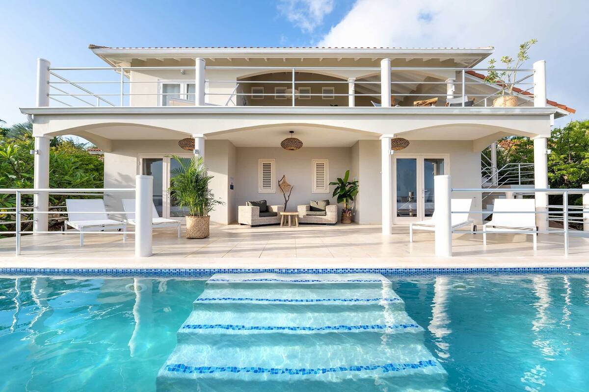 Ein zweistöckiges Haus mit Swimmingpool, Sitzgelegenheiten im Freien und einer überdachten Terrasse.