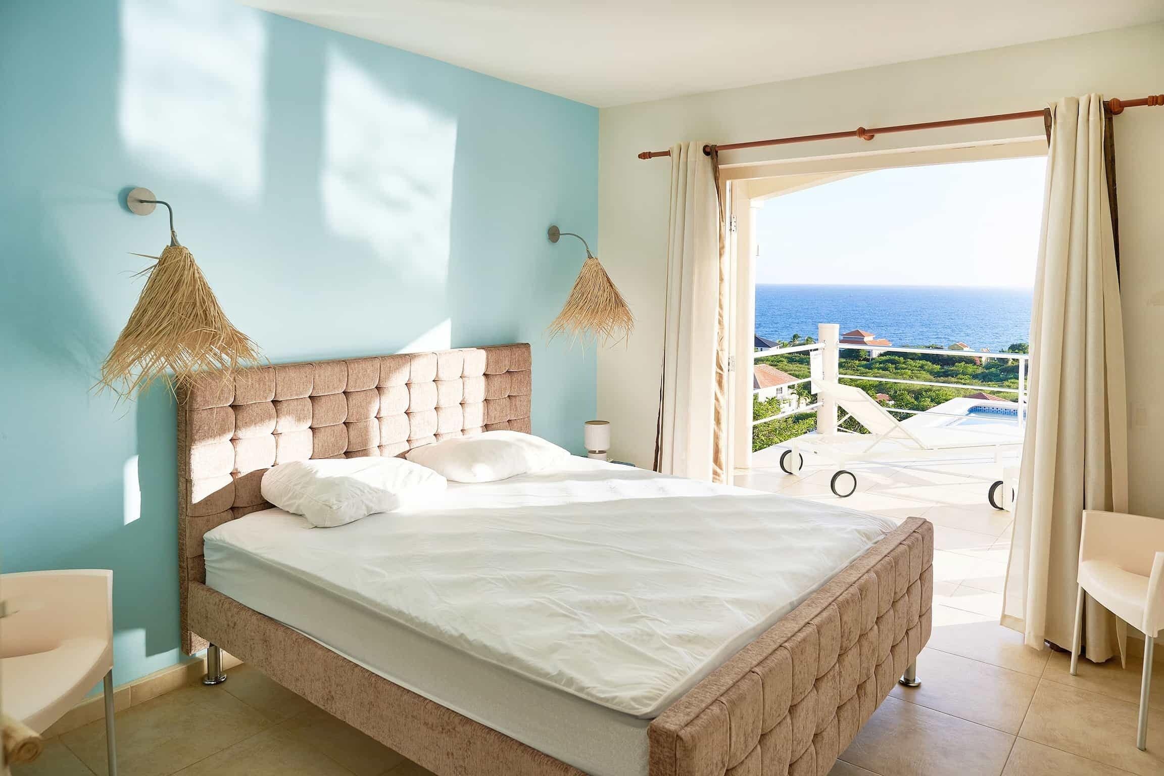 A bedroom with a large bed, a view of the sea, and a balcony with outdoor furniture.