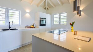 A modern kitchen with white cabinetry, a central island, and built-in appliances. - Coral Estate Rentals (St. Marie)