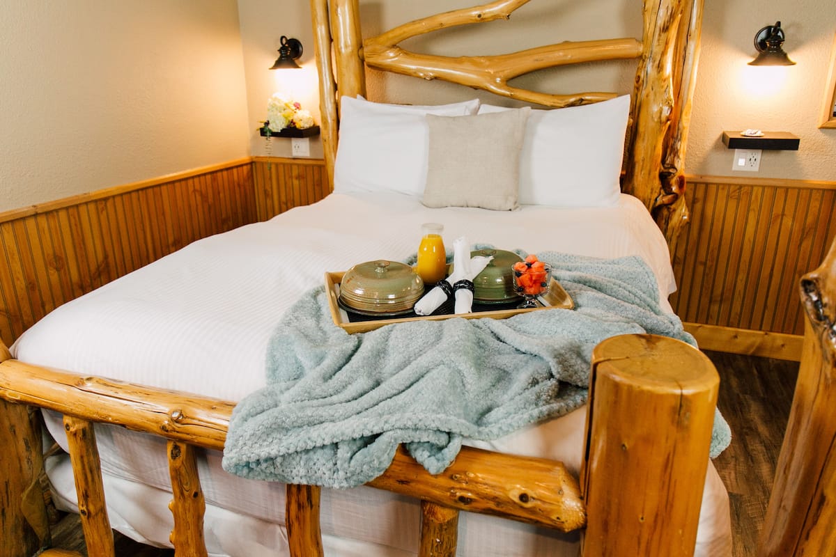 A wooden-framed bed with a tray of breakfast items, a blue blanket, and a wooden headboard.
