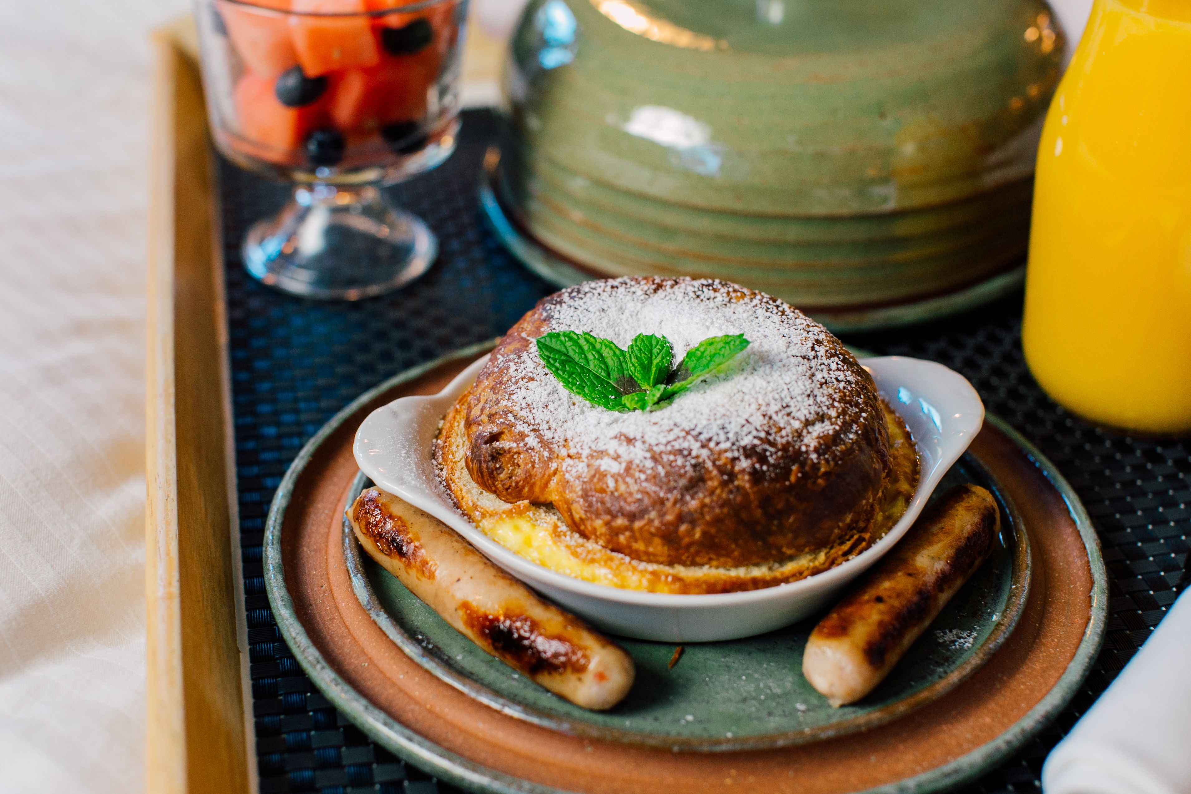 A dessert plate with a pastry, two sausages, and a green pot in the background.