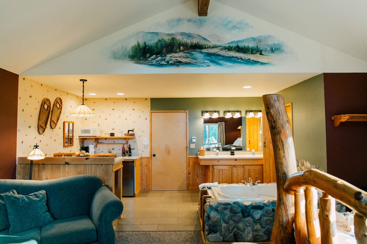 A cozy kitchen with wooden cabinets, a dining area with a blue sofa, and a bathroom with a stone bathtub.