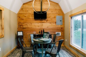 A wooden-paneled room with a round table, chairs, a flat-screen TV, and a window with a view of trees. - Pine River Ranch B&B (Leavenworth)