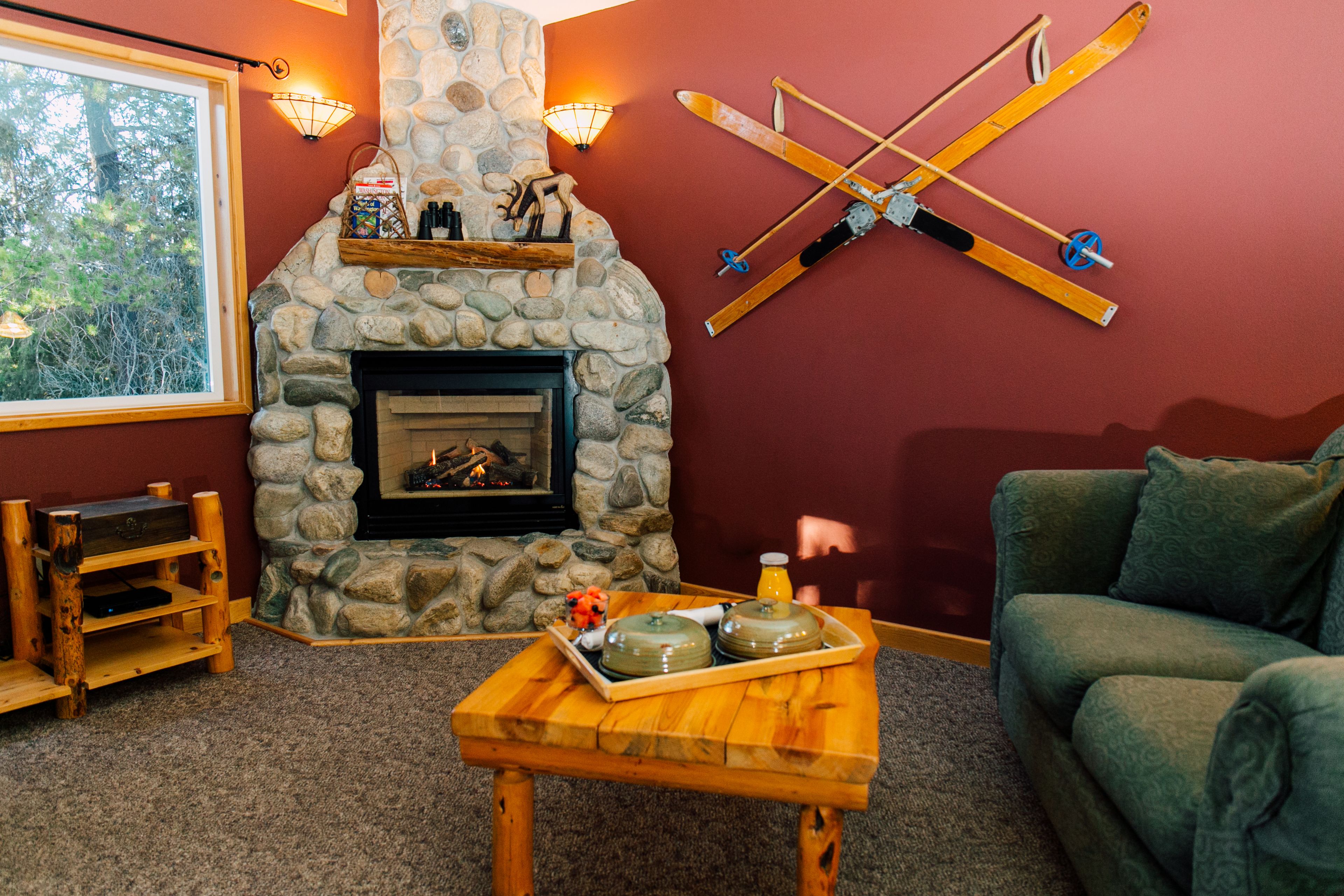 Un salón acogedor con chimenea de piedra, una mesa de centro de madera con objetos decorativos, un sofá verde y un perchero para esquíes fijado a la pared.
