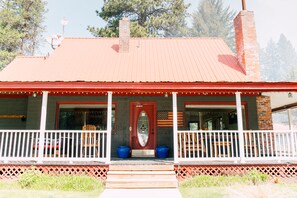 A two-story house with a red roof, a front porch with white railings, and a brick chimney. - Pine River Ranch B&B (Leavenworth)