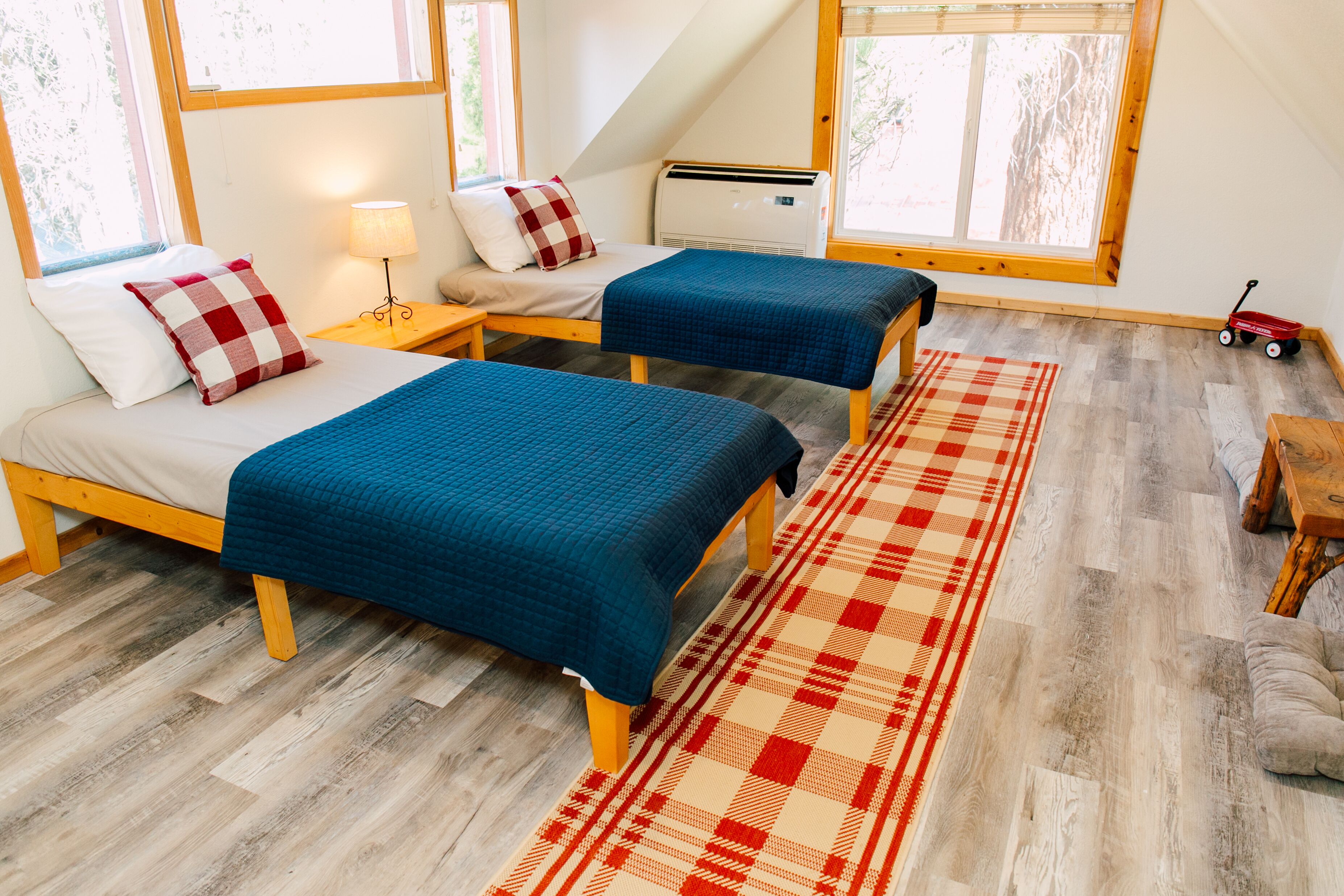 A room with two beds, a red and white checkered rug, and a wooden floor.