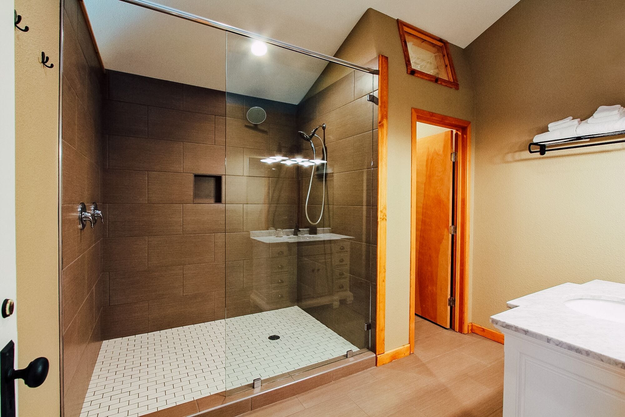 Un baño moderno con ducha envuelta en vidrio, puerta de madera y lavamanos blanco.