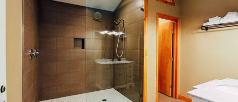 Un baño moderno con ducha envuelta en vidrio, puerta de madera y lavamanos blanco.
