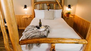 A wooden-framed bed with a bottle and glasses on the side, a blanket, and a small plant on a nightstand.