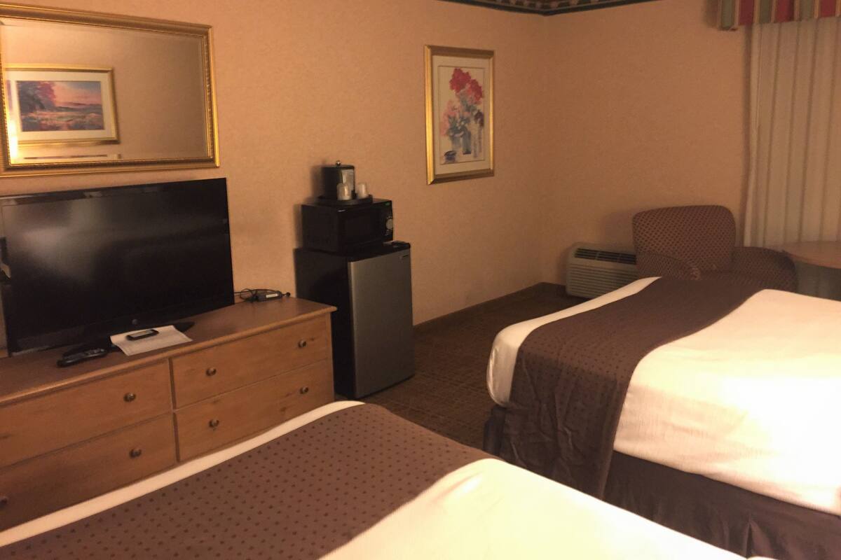 A hotel room with two beds, a TV, a dresser, a microwave, and a painting on the wall.