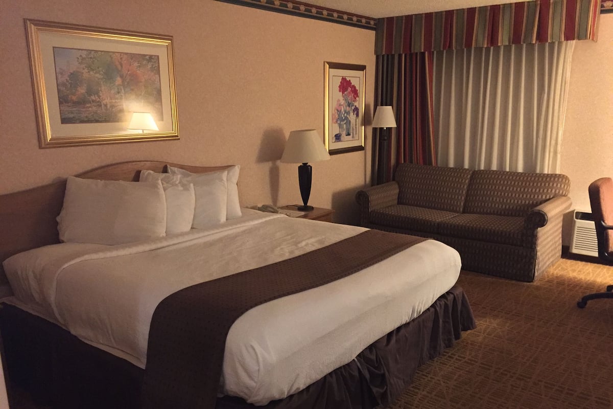 A hotel room with a large bed, a sofa, two lamps, and two framed pictures on the walls.
