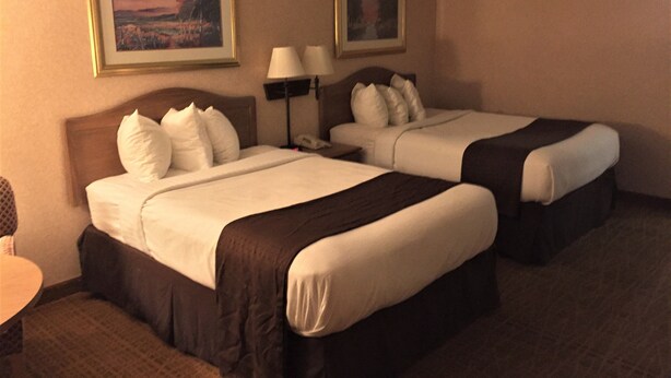 A hotel room with two beds, a desk, and two framed pictures on the wall. - Americas Best Value Inn & Suites Boise (Boise)