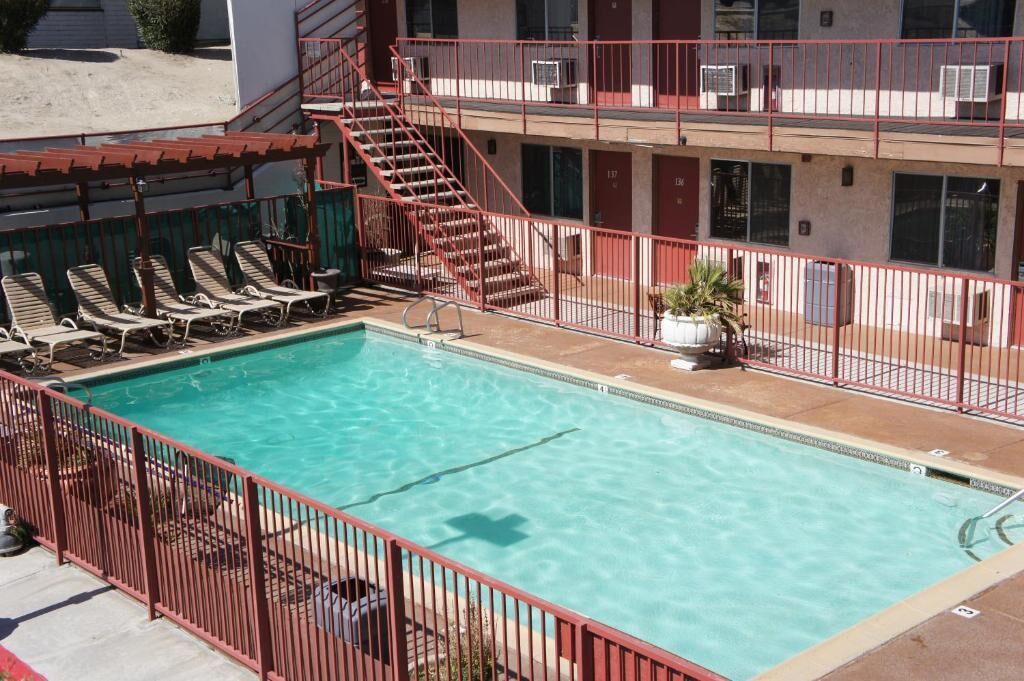 A pool with sun loungers, a staircase, and a building with multiple windows and air conditioning units.