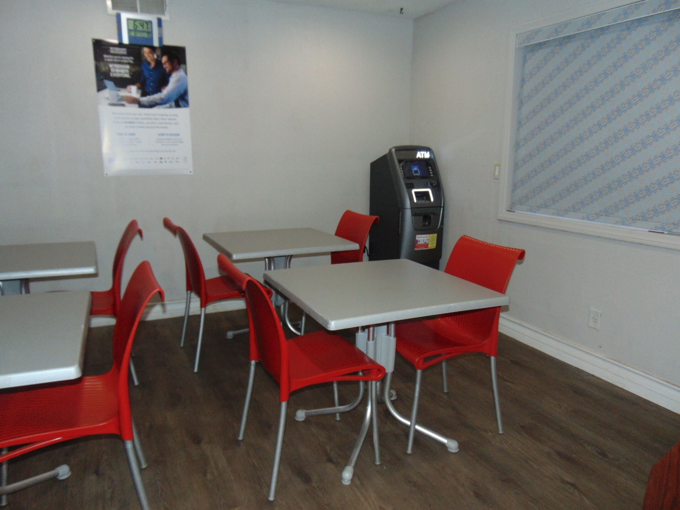 A room with tables and chairs, a vending machine, and a window with patterned curtains.
