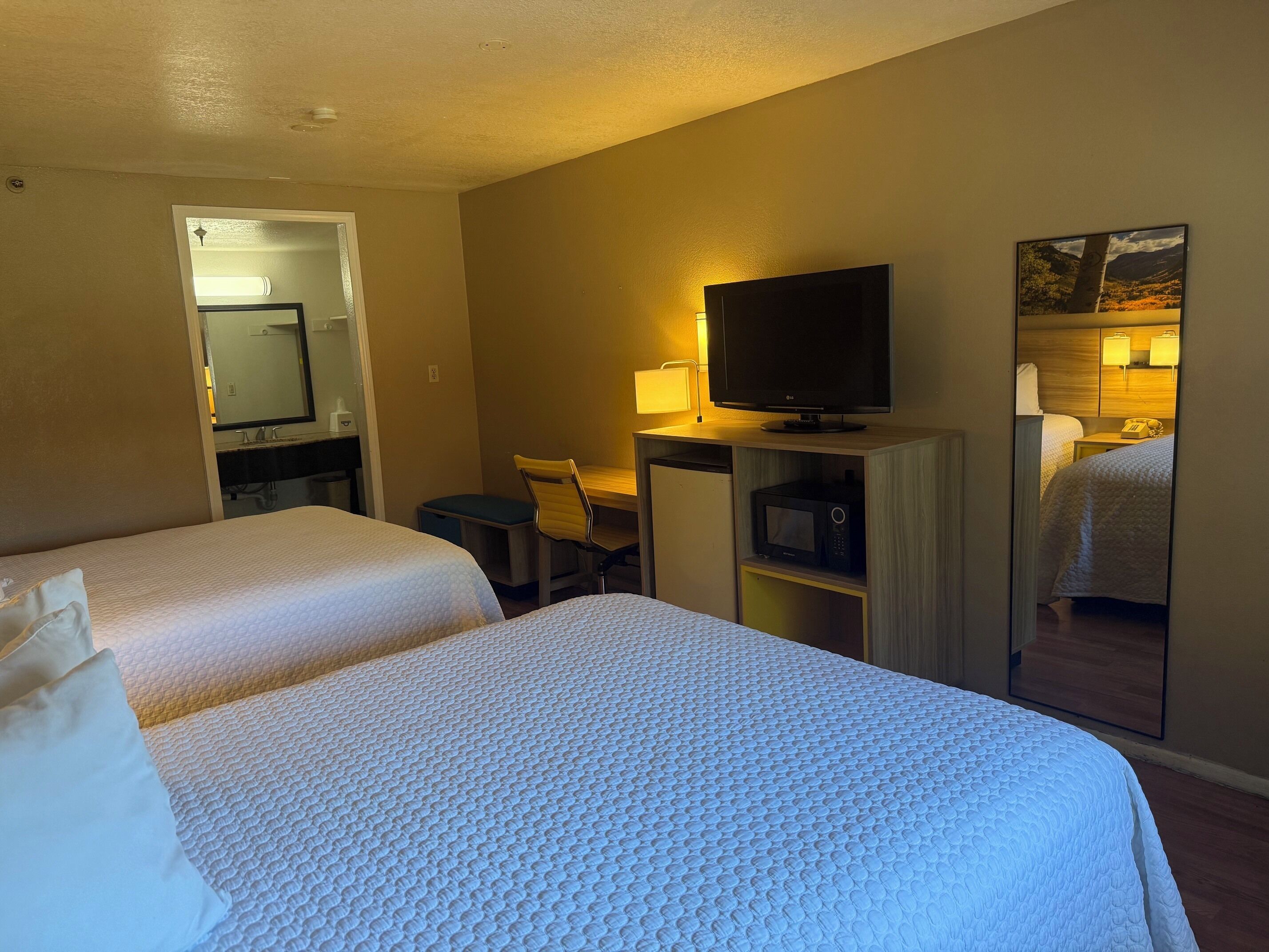 A hotel room with two beds, a desk with a TV, a microwave, and a mirror.