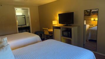 A hotel room with two beds, a desk with a TV, a microwave, and a mirror.