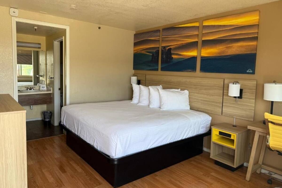 A hotel room with a large bed, a wooden headboard, a bedside table, a nightstand, a mirror, and a wall-mounted artwork.