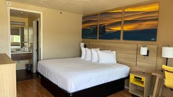 A hotel room with a large bed, a wooden headboard, a bedside table, a nightstand, a mirror, and a wall-mounted artwork.
