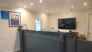 A reception area with a dark wood paneling wall, a flat-screen TV mounted above a counter, and a clock on the wall. - Days Inn by Wyndham Victorville/Hesperia I-15 & Palmdale Rd (Victorville)