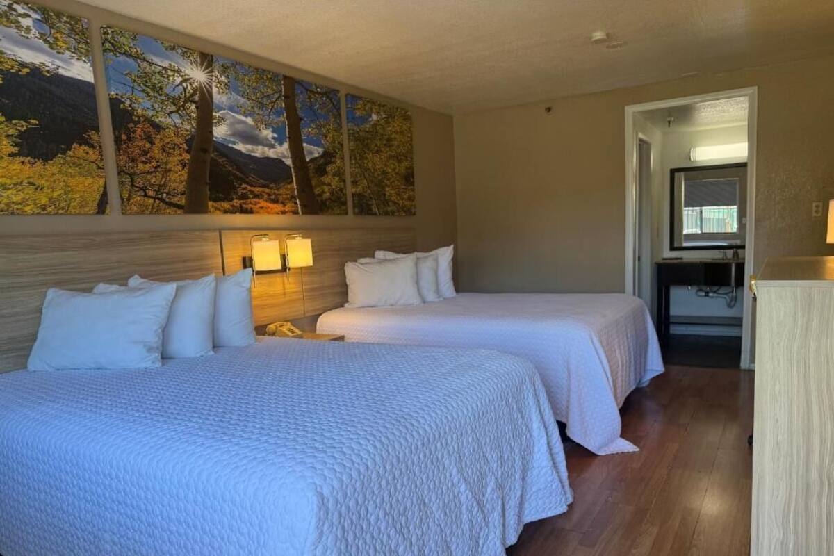A hotel room with two beds, a large painting on the wall, a desk with a lamp, and a view of the mountains.