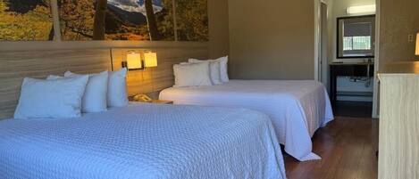 Habitación de hotel con dos camas, un cuadro grande en la pared, un escritorio con lámpara y vistas a las montañas.