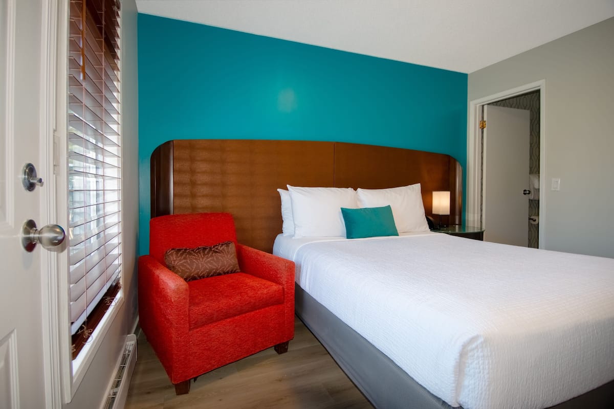 A hotel room with a large bed, a red armchair, and a teal accent wall.