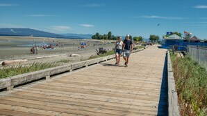 Un malecón de madera que conduce a una playa con gente y tiendas de campaña.