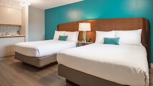 Habitación de hotel con dos camas, una mesita de noche con lámpara, una pequeña mesa con teléfono y un baño con espejo y toallero.