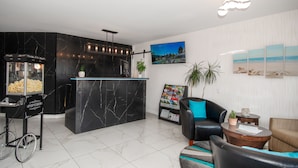 Un vestíbulo moderno con un mostrador de recepción de mármol, un carrito de palomitas, una zona de estar con sillones de cuero y un televisor montado en la pared.