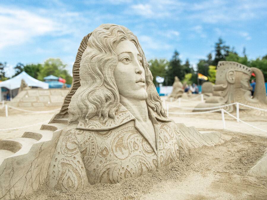 A detailed sand sculpture of a figure with intricate patterns and a rope barrier around it.
