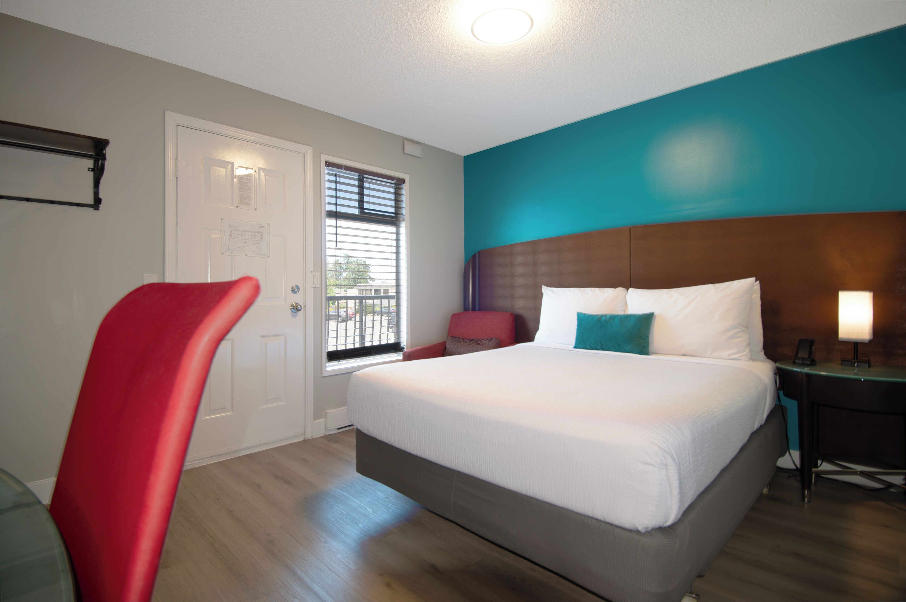 Une chambre d’hôtel avec un lit, un bureau, une chaise, une porte et une fenêtre.