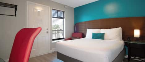A hotel room with a bed, a desk, a chair, a door, and a window.
