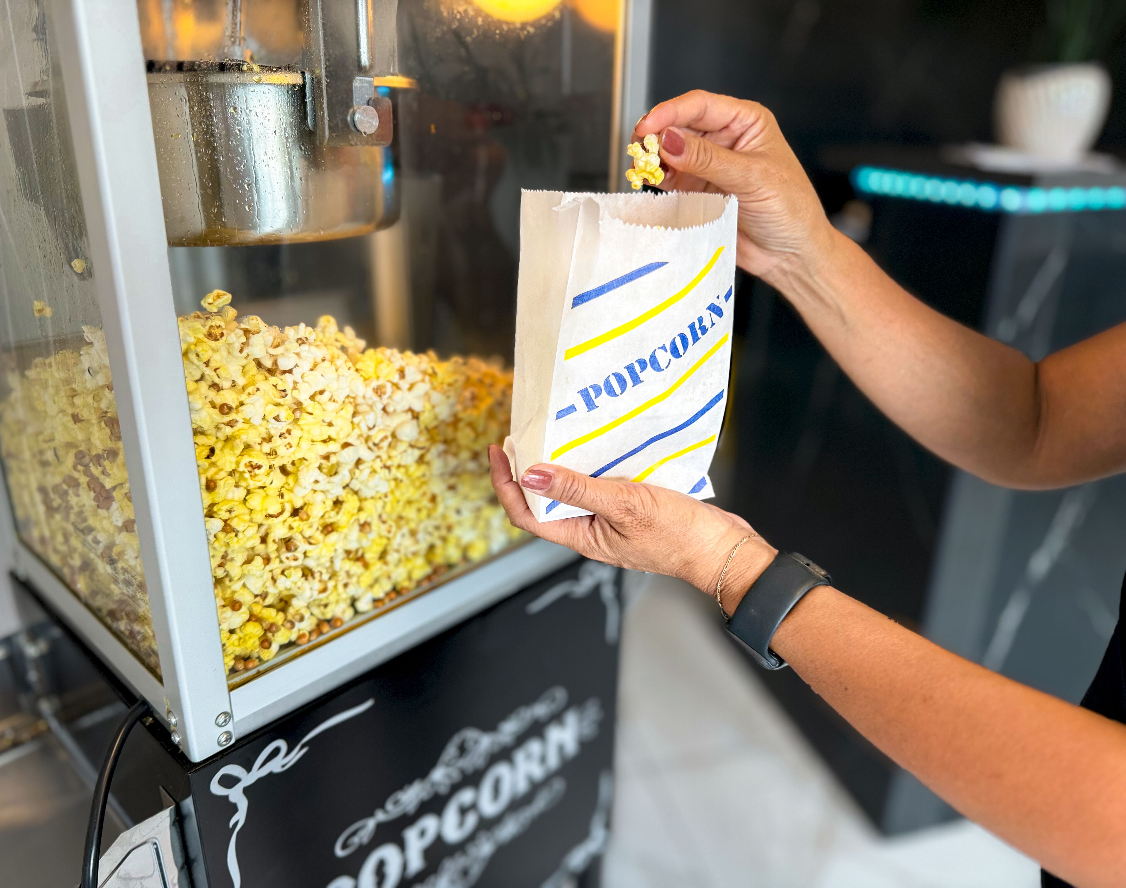 A person holding a bag of popcorn from a machine labeled "Popcorn".