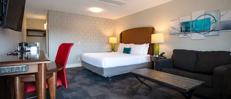 A hotel room with a bed, a desk, a red chair, a sofa, and a coffee table.
