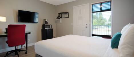 A bedroom with a bed, a desk, a chair, a TV, a door, and a window.