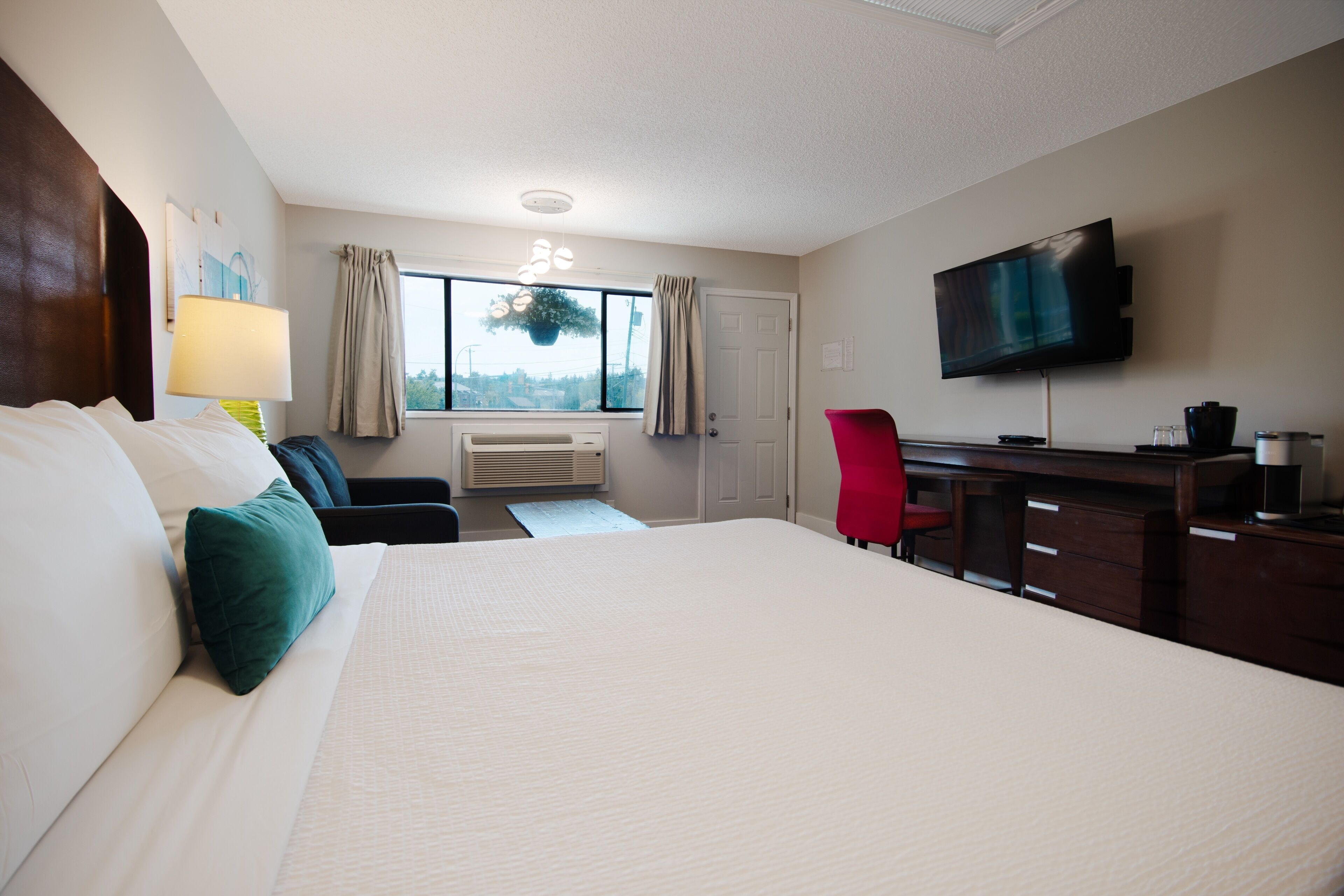 A hotel room with a large bed, a desk with a chair, a TV, and a window with curtains.