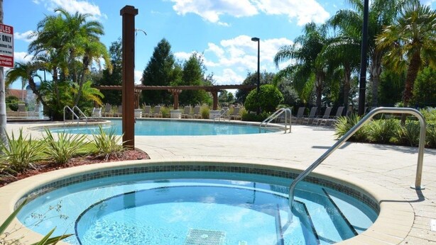 Un área de piscina con dos jacuzzis, rodeada de palmeras y tumbonas.