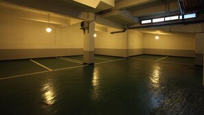 An indoor parking garage with concrete pillars, fluorescent lighting, and a green floor. - Prince Hotel (Seoul)