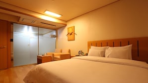 A hotel room with a large bed, a seating area with a chair and a table, a wardrobe, and a sliding door closet. - Prince Hotel (Seoul)