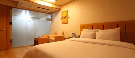 A hotel room with a large bed, a seating area with a chair and a table, a wardrobe, and a sliding door closet.