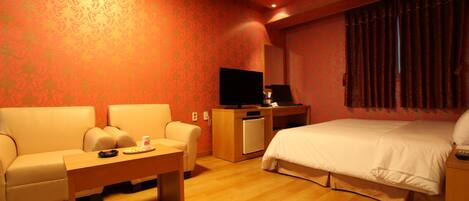 Una habitación de hotel con sofá, cama, escritorio, televisión y un refrigerador pequeño.