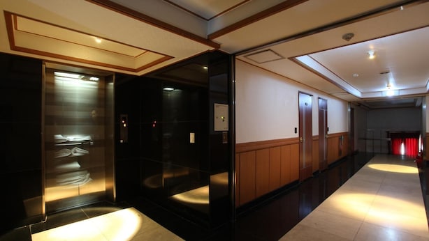 A hotel corridor with a glass elevator, wooden panel walls, and a red curtain at the end. - Prince Hotel (Seoul)