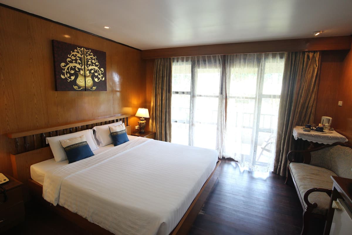 A hotel room with a large bed, a bedside table with a lamp, a chair, and a window with curtains.