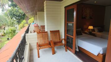 A balcony with wooden chairs, a bed with white bedding, and a view of greenery.
