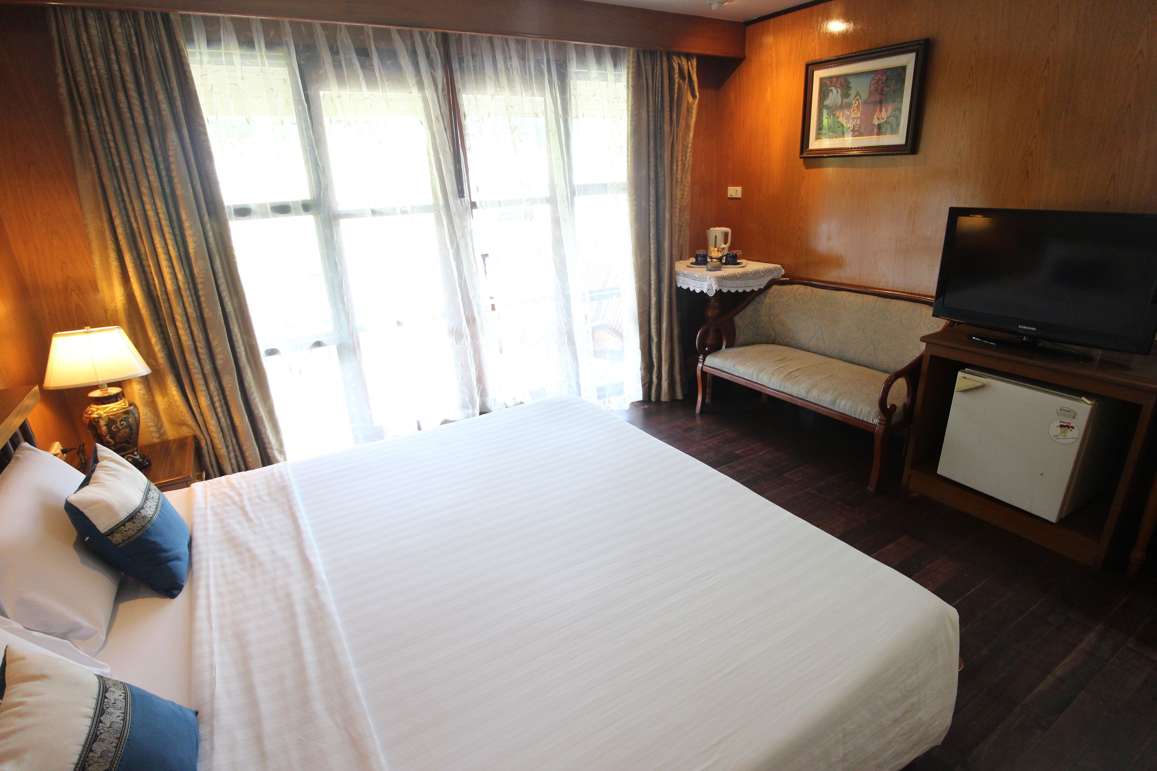 A hotel room with a large bed, a television, a small table with a lamp, and a chair.