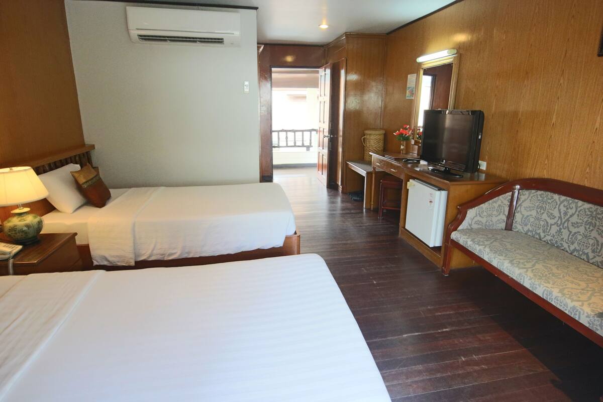 A hotel room with two beds, a desk with a television, a sofa, and a small cabinet.
