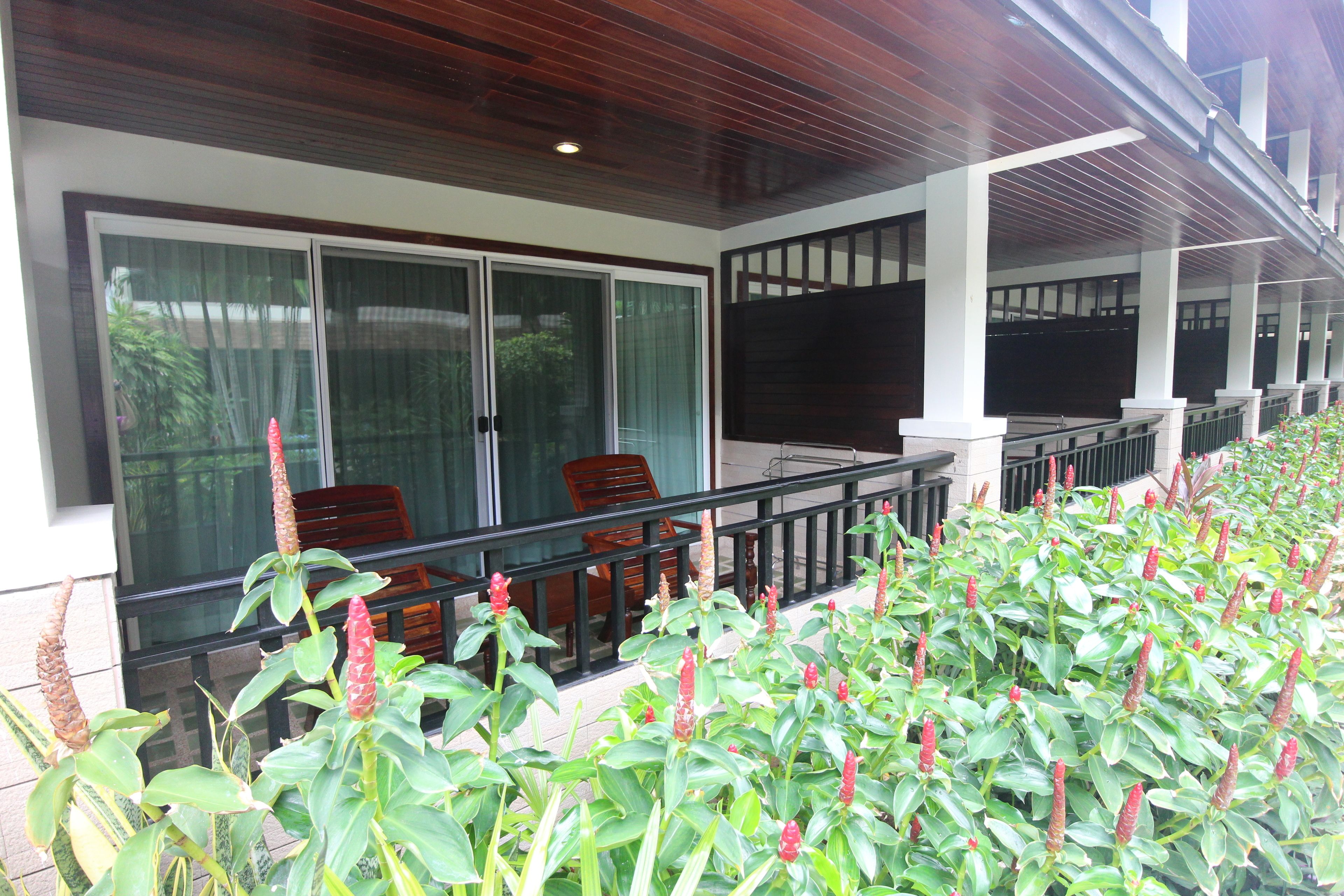 A covered outdoor seating area with a glass partition, wooden chairs, and a view of the building's interior.